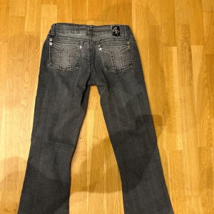 Grå bootcut jeans från Gina Tricot - Snygga grå jeans från Gina Tricot med bootcut passform och slitna detaljer på benen. Jeansen har låg midja, klassiska fem fickor och dragkedja. Materialet är mjukt denim med lite stretch för extra komfort.