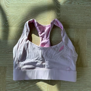 Ljusrosa sporttopp från Stronger - Sporttopp i ljusrosa från Stronger med brottarrygg och bred resår under bysten. Tillverkad i mjukt och stretchigt material som passar perfekt för träning. Diskret logga framtill i rosa. Snygg och bekväm för aktiva dagar.