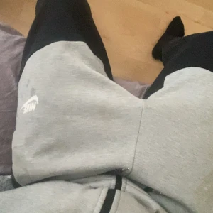 Nike grå och svarta mjukisbyxor - Snygga mjukisbyxor från Nike i grått och svart med vit logga på låret. Byxorna har dragsko i midjan och är tillverkade i mjukt bomullsmaterial. Perfekta för chill eller träning, 