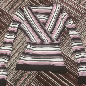 Randig omlott-tröja i rosa och brunt - Supersnygg omlott-tröja med smickrande v-ringning och långa ärmar. Tröjan har ett randigt mönster i rosa, brunt och vitt och sitter figurnära. Perfekt till jeans eller kjol för en trendig look. Materialet är stickat och känns mjukt mot huden. Köpte från Humana.