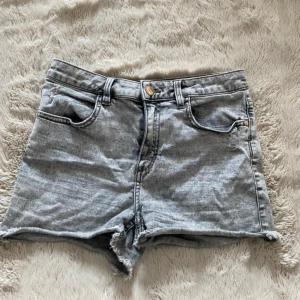 Grå jeansshorts  - Snygga grå jeansshorts. Klassisk femficksmodell med dragkedja och knapp framtill. Perfekta för sommaren och ger en avslappnad vibe. Lätt slitna detaljer på bakfickan för extra edge.