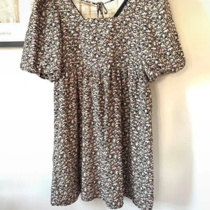 Stylish klänning strl S från Studio, Only  - En supersnygg och stylish klänning i strl S från Onlys kollektion Studio. Halsmynningen på framsidan är i raka linjer formade som en rektangel och ger en mycket snygg framtoning. Bak på ryggen är den formad på liknande sätt men man har även två band att knyta för bästa möjliga passform. Ärmarna är i puffmodell med resår i ärmsluten. Den är tillverkad helt i polyester och har en isydd underklänning som gör att den blir extra snygg i fallet och känns som en dyrare modell. Använd 2-3 gånger 