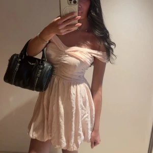 Ljusrosa offshoulder kortklänning - Supersöt ljusrosa kortklänning med offshoulder och lätt puffig kjol. Klänningen har en omlottliknande överdel och markerad midja. Perfekt för sommarens alla tillfällen! säljer pågrund utav den ej kommer till användning längre. storlek S men passar även XS