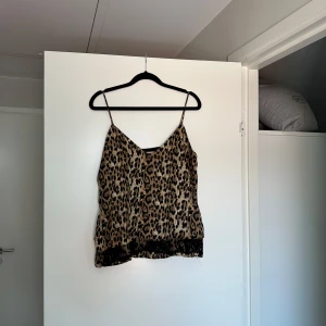 Leopardmönstrad linnetopp från Zara - Säljer en snygg leopardmönstrad linnetopp från Zara Basic i storlek S. Toppen har tunna axelband, v-ringning och svart spetsdetalj längst ner. Materialet är glansigt och lätt, perfekt för att sticka ut med ett djurmönster.