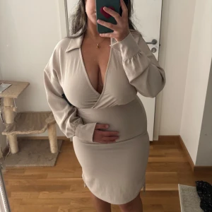 Beige omlottklänning med krage - Snygg beige kortklänning från Nelly i storlek 36🩷Man kan justera sidorna med banden på varsin sida av klänningen🤍 Klänningen är helt oanvänd och har enbart testats✨