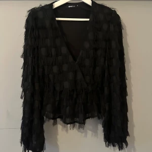 Svart fransig cardigan jacka Gina Tricot - Svart cardigan jacka från Gina Tricot med cool fransig struktur och diskreta prickar i tyget. Jackan är lätt och transparent, har v-ringning och långa ärmar. Perfekt för dig som vill sticka ut med en unik och trendig look.