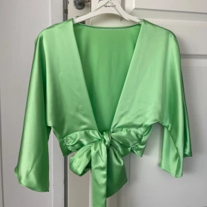Grön satin topp med knyt från Zara - Snygg ljusgrön bolerotopp i satin med trekvartsärmar och djup v-ringning. Toppen har långa knytband framtill som ger en cool omlott-look. Aldrig använd. Den är från Zara. Kommer inte kunna skicka mer bilder än detta. Storlek M men passar en storlek Xs-S också. 