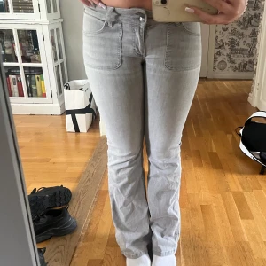 Ljusgrå bootcut jeans med fickor - Säljer ett par ljusgrå jeans med bootcut-snitt och låg midja. Byxorna har även bakfickor med knapp och klassisk jeansknäppning. Snygg passform och perfekt till en trendig vardagslook. Märket är Nelly och är i storlek 38