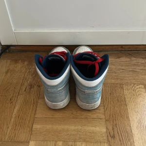 Nike Air Jordan 1 Mid blå/vit/röd - Säljer ett par Nike Air Jordan 1 Mid i blått och vitt med röda skosnören och detaljer. Skorna har klassisk Jordan-logga på plösen och sidan, samt grå Swoosh. Ovandel i mocka och skinn, insida i blå textil. Perfekt för dig som vill sticka ut med färg! Skicket är Sparsamt använda, prutat och klart.