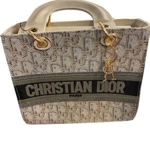  beige handväska - Snygg handväska i beige och grått  Väskan har kraftiga handtag i ljus skinn och detaljer i guldmetall. Perfekt för dig som vill sticka ut med lyxig design.