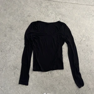 Svart långärmad topp Gina Tricot S - En svart långärmad topp från Gina Tricot i storlek S. Toppen har en rundad halsringning och är tillverkad i ett mjukt, stretchigt material. Ärmarna har en snygg slitsdetalj som ger en extra touch till looken. Perfekt att styla med jeans eller kjol.