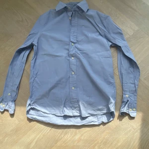 Blå skjorta från Ralph Lauren - Klassisk blå skjorta från Ralph Lauren med broderad logga på bröstet. Skjortan har lång ärm, knappar framtill och är tillverkad i ett tunt bomullstyg. Perfekt för dig som gillar stilren och tidlös design. Tveka inte på att höra av dig!!!