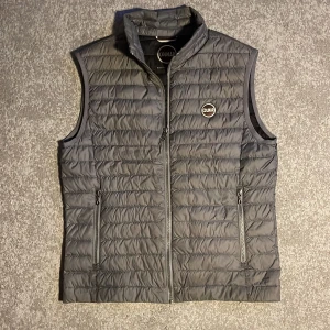 Colmar väst - En grå Colmar dunväst som är i fint skick! Det är storlek S. Västen har dock en pytteliten skada längst ner åt vänster om man tittar på första bilden, (hela märket på sista bilden). Men märket syns inte om man inte kollar noga! Skicka gärna om ni har frågor eller om ni vill ha andra bilder! 