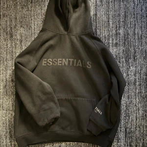 Svart hoodie från Essentials - Säljer en svart hoodie från Essentials med texten 'ESSENTIALS' tryckt på framsidan. Hoodien har en rymlig passform och en stor ficka framtill. 