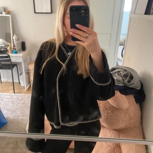 Svart kofta med vita sömmar från Gina Tricot - Säljer en svart tröja från Gina Tricot med kontrasterande vita sömmar. Tröjan har en lös passform och långa ärmar, perfekt för en avslappnad stil. Den är tillverkad i ett mjukt material som känns skönt mot huden.