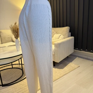 Vita stickade byxor med snörning - Snygga vita stickade byxor med en bekväm passform och snörning i midjan. Byxorna har ett flätat mönster längs sidorna som ger en extra touch. Perfekta för en mysig dag hemma eller en avslappnad dag ute. Passar perfekt som oversize modell (s/m/l storlek). 🌸👌