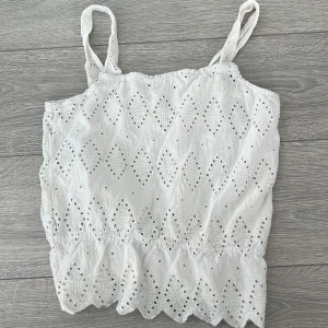 Vit broderad linnetopp från Pimkie - Säljer en söt vit linnetopp från Pimkie med broderade detaljer och justerbara axelband. Perfekt för varma sommardagar med sitt luftiga och lätta material. Toppen har en elastisk nederkant för en bekväm passform.