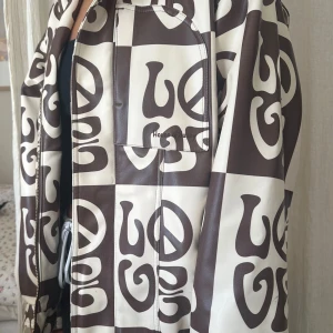 Brun och vit mönstrad jacka från house of sunny - Säljer en unik brun och vit jacka med ett iögonfallande mönster av ordet 'LOVE' och fredssymboler. Jackan har en dragkedja framtill och en normal passform och är från house of sunny i storlek 36 (skulle säga att den är over size). Perfekt för att sticka ut i mängden! Väl använd🤍