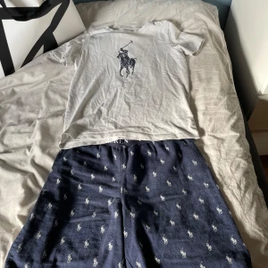 Vit t-shirt och shorts från Ralph Lauren - Säljer en klassisk vit t-shirt från Ralph Lauren med en stor svart polospelare tryckt på framsidan. T-shirten har en normal passform och korta ärmar. Perfekt för en stilren och avslappnad look.