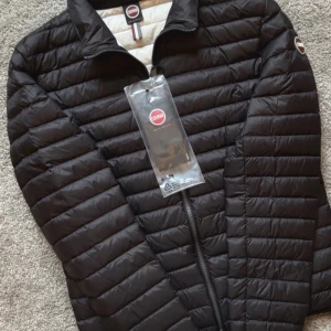 Svart pufferjacka från Colmar - Snygg svart pufferjacka från Colmar med dragkedja och quiltad design. Jackan har en diskret logga på ärmen och är perfekt för kyligare dagar. Insidan är ljus och kontrasterar snyggt mot den mörka utsidan. Helt ny aldrig använd ny priset är 4500kr alls lappar o prislapp finns kvar👍
