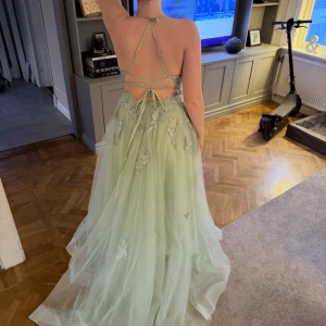 Grön långklänning med spetsdetaljer - Elegant grön långklänning med öppen rygg och vackra spetsdetaljer. Klänningen har tunna axelband som korsas i ryggen och ger en romantisk känsla. Perfekt för speciella tillfällen.