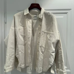 Beige jacka från Zara - Säljer en stilren beige jacka från Zara. Skjortan har en avslappnad passform med knappar framtill och två stora bröstfickor. Perfekt för lager-på-lager-stil.