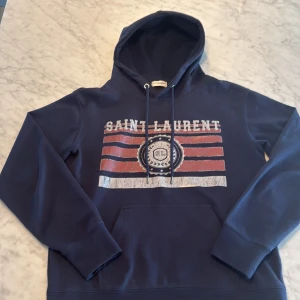 Mörkblå hoodie från Saint Laurent -  Mörkblå hoodie från Saint Laurent. Väldigt bra skick i storleken S, mitt pris 3500kr nypris runt 7000kr