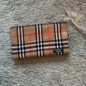 Cashmere Halsduk från Burberry - 100% ÄKTA! Säljer en SNYGG klassisk rutig halsduk från Burberry i beige, svart, vit och röd. Den är tillverkad i mjuk kashmir och har fransar i ändarna. Perfekt för att hålla sig varm och stilren under kyliga dagar. Pris kan diskuteras. Passar för alla! Mycket Bra Skick. Originalpris:5500 Vårt pris 299! Kontakta för funderingar🤗