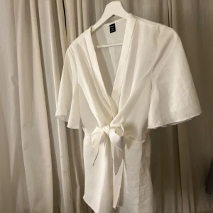 Vit omlottklänning med knyt - Elegant vit omlotttopp med knyt framtill och korta ärmar. Använd 1 gång, kommer inte till användning. 