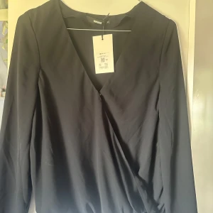 Svart omlottblus från Bik Bok - Snygg svart omlottopp från Bik Bok med v-ringning och långa ärmar. Aldrig använd. Prislappen finns kvar. Nypris 359.