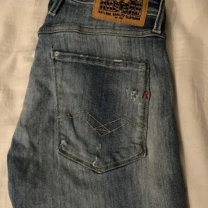 Blå jeans från Replay - Säljer ett par blå Replay Anbass jeans med slitna detaljer och en cool, avslappnad look. De har en knappgylf och klassisk femficksdesign. Perfekta för en trendig stil! Priset kan diskuteras 