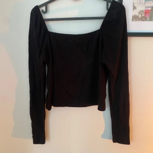 Lindex svart ribbad topp - Snygg svart ribbad topp med långa ärmar och en elegant fyrkantig halsringning. Perfekt för en stilren look.
