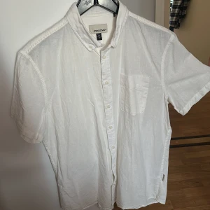 Vit kortärmad skjorta från Blend - Säljer en stilren vit kortärmad skjorta från Blend. Skjortan har en klassisk krage och knappar framtill. Den är tillverkad i ett lätt och bekvämt material, perfekt för varma dagar. En bröstficka ger en extra touch till designen.