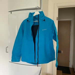 Turkos vindjacka från Everest - Säljer en turkos vindjacka från Everest med dragkedja och justerbara ärmslut. Perfekt för utomhusaktiviteter med sin funktionella design och bekväma passform. Jackan har en stilren look och är idealisk för blåsiga dagar.