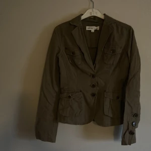 Olivgrön kavaj från Sara Kelly - Snygg olivgrön kavaj från Sara Kelly by Ellos med knappar framtill och fickor med lock. Perfekt för en stilren look. Kavajen har långa ärmar och en klassisk krage.