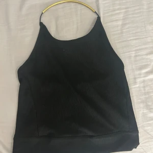 Svart ribbad linnetopp från NLY Design - Snygg svart ribbad linnetopp från NLY Design. Toppen har en  guldfärgad detalj vid halsen. Perfekt för att styla med både jeans och kjol.