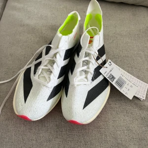 Sprintskor från Adidas - Säljer ett par vita och svarta sprintskor från Adidas med snörning och en iögonfallande rosa sula. Skorna har en stabil klack framtill och är bra dämpade och stabila.  Perfekta för den seriösa friidrottaren. Helt nya! Aldrig använda!