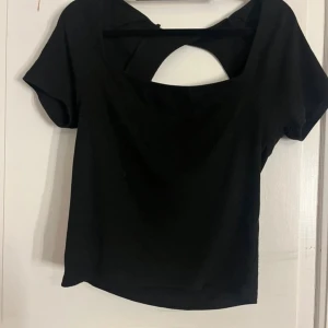 Svart topp med öppen rygg - Snygg svart topp med korta ärmar och en stilren öppen ryggdetalj. Perfekt för en kväll ute eller en avslappnad dag. Enkel att matcha med olika outfits.