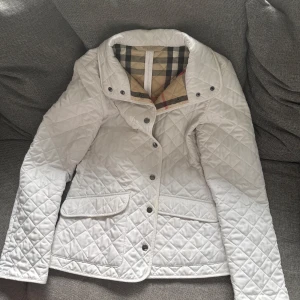Burberry Brit jacka  - Säljer en stilren vit quiltad jacka från Burberry med klassiskt rutigt foder. 