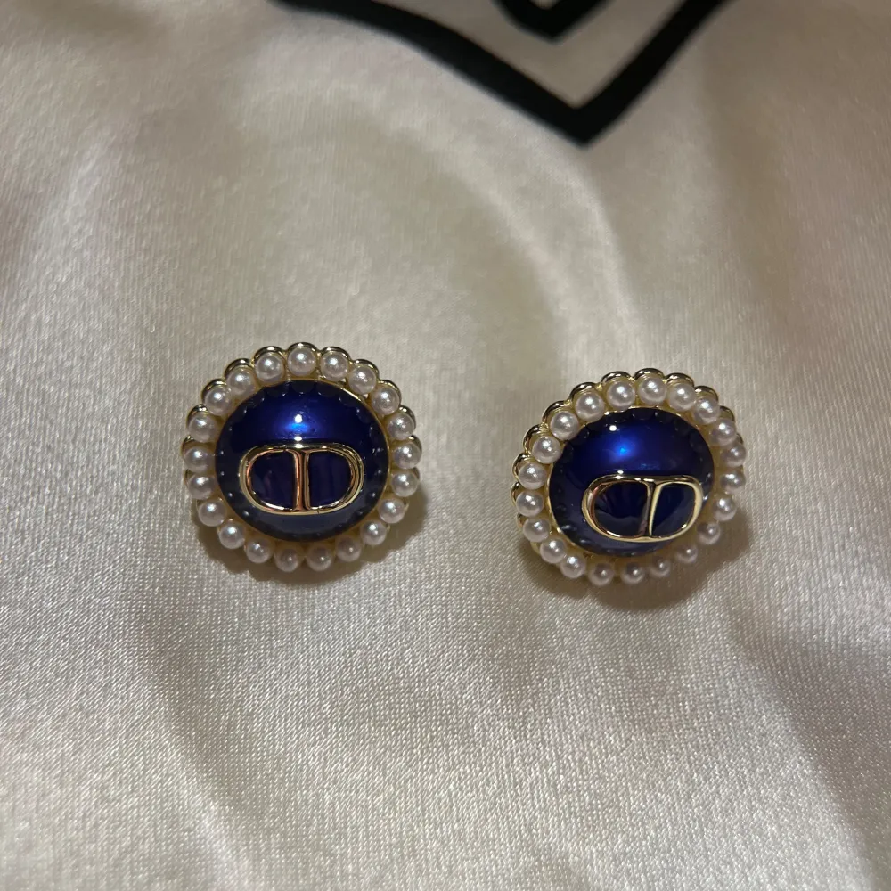 Snygga örhängen med en djupblå mitt och en ram av små pärlor. De har en elegant design med guldfärgade detaljer i mitten. Perfekta för att ge en touch av lyx till din outfit.. Asusteet.
