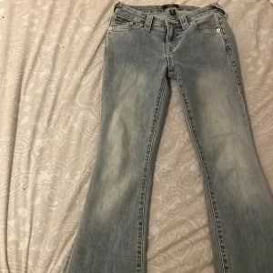Ljusblå bootcut jeans från True Religion - Säljer ett par ljusblå bootcut jeans från True Religion i modellen Becca. De har en medelhög midja och snygga detaljer med knappar på bakfickorna. 