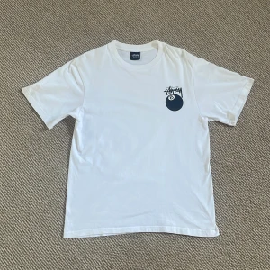 Vit t-shirt från Stussy - Säljer en klassisk vit t-shirt från Stussy i storlek S. T-shirten är tillverkad i 100% bomull. På Framsidan av tröjan bredvid ena armen är det en liten fläck men den märks knappt. 