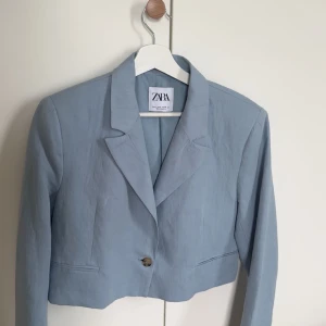 Ljusblå kavaj från Zara - Snygg ljusblå kavaj från Zara med en enkel knapp framtill. Kavajen har en klassisk krage och är croppad i modellen. Perfekt för en stilren look.