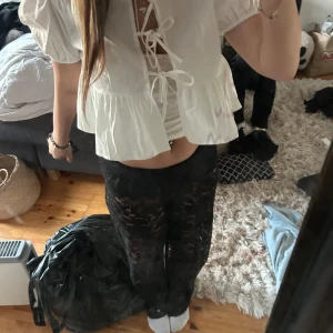 Vit blus med snörning - Säljer en söt vit blus med korta ärmar och snörning framtill. Blusen har volangdetaljer vid ärmslut och nederkant, vilket ger en romantisk touch. Perfekt för en somrig look!