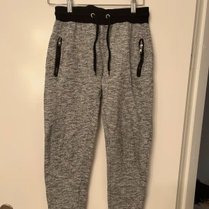 Grå mjukisbyxor med svarta detaljer - Snygga grå mjukisbyxor med svarta dragkedjor och snörning i midjan. Byxorna har ribbade muddar vid bensluten och en bekväm passform. Köpt på tjejavdelning men snygg på alla, därav unisex!