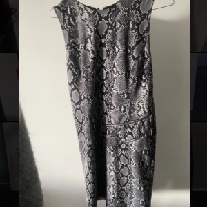 Ormmönstrad klänning från Michael Kors - Snygg ärmlös klänning från Michael Kors med ett coolt ormmönster i svart och grått. Klänningen har en dragkedja på sidan för enkel på- och avtagning. Perfekt för att sticka ut med stil!