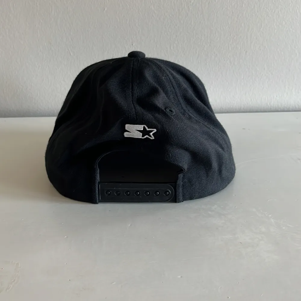 Snygg svart keps från DC med vit broderad logga framtill. Kepsen har en justerbar baksida för perfekt passform. Tillverkad av en blandning av akryl och ull, vilket ger en skön känsla. Perfekt för en casual look.. Asusteet.