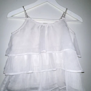 Vit linnetopp från Uniq Young - Säljer en söt vit linnetopp från Uniq Young med volangdetaljer. Toppen har tunna axelband och ett luftigt, flödande tyg som ger en lätt och somrig känsla. Perfekt för varma dagar!