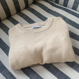 Stickad tröja - Snygg stickad tröja ifrån Zara i bra skick med en liten defekt på ärmen. Tröjan är ljus beige och passar perfekt inför våren och i sommaren till ett par ljusa jeans.