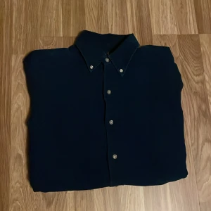 Mörkblå skjorta från Ralph Lauren - Säljer en stilren mörkblå skjorta från Ralph Lauren i slim fit. Skjortan har knappar framtill och en klassisk krage. Den är broderad med Ralph Laurens ikoniska logga på bröstet. Perfekt för en elegant look. Kolla gärna in butiken, möjlighet på bundle finns.
